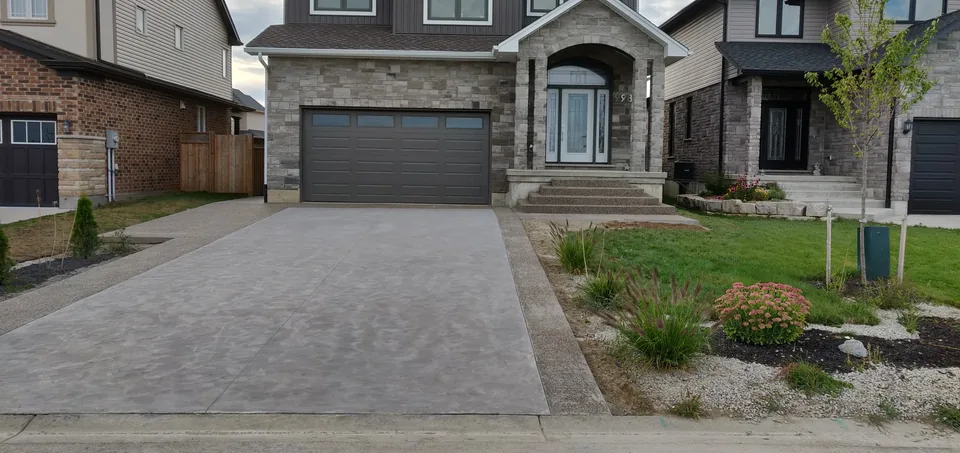 A textured concrete driveway with darker borders leading to a double garage.