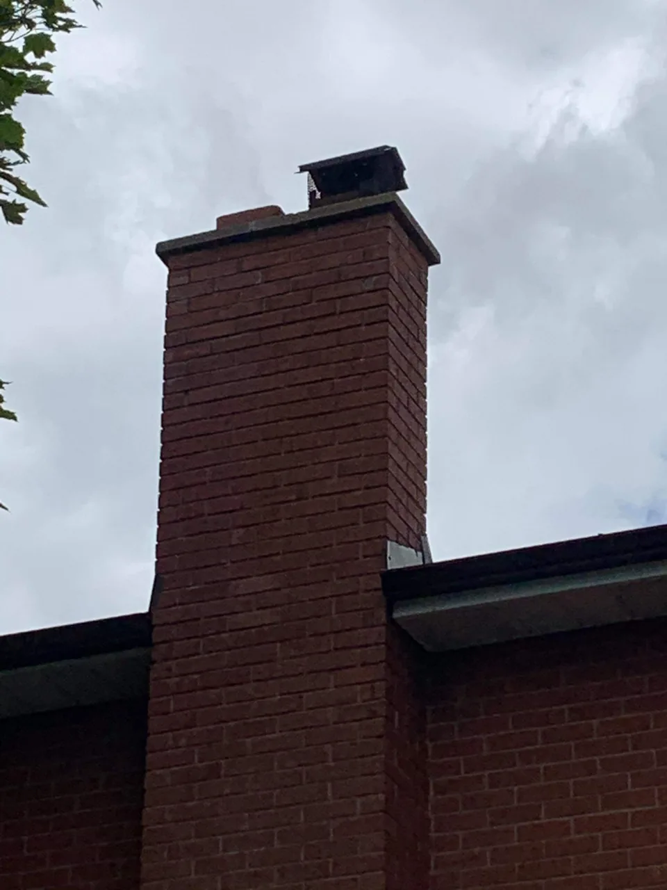 A tall red brick chimney rises above the edge of a roof against an overcast sky.