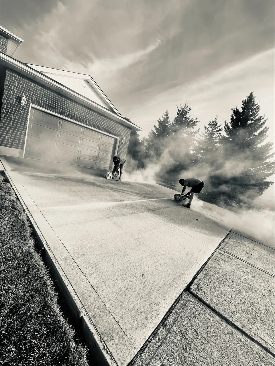 A monochrome photograph of two crew members using concrete saws on a driveway.