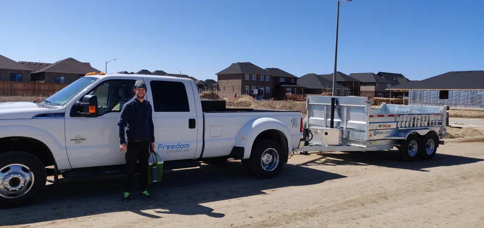 A crew member stands beside a white Freedom Concrete truck and equipment trailer.