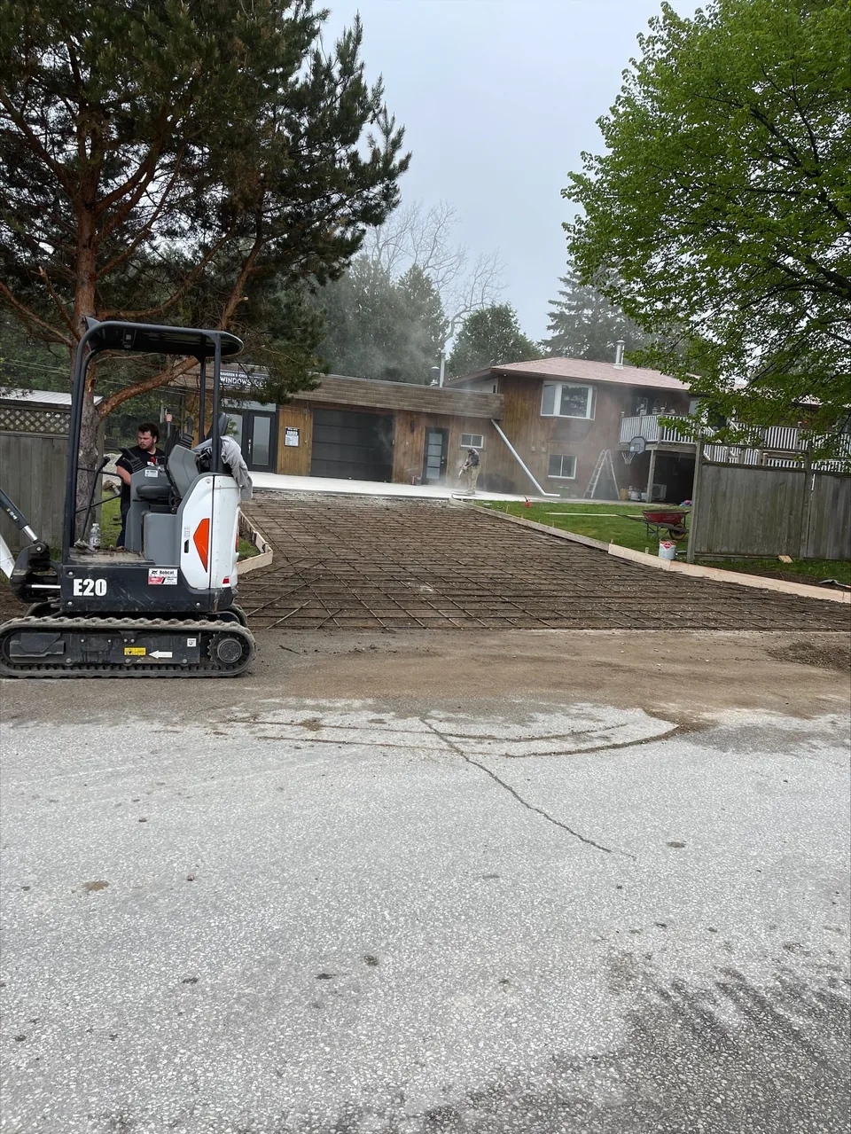 Steel reinforcing mesh and timber forms are laid out for a driveway beside a compact excavator.