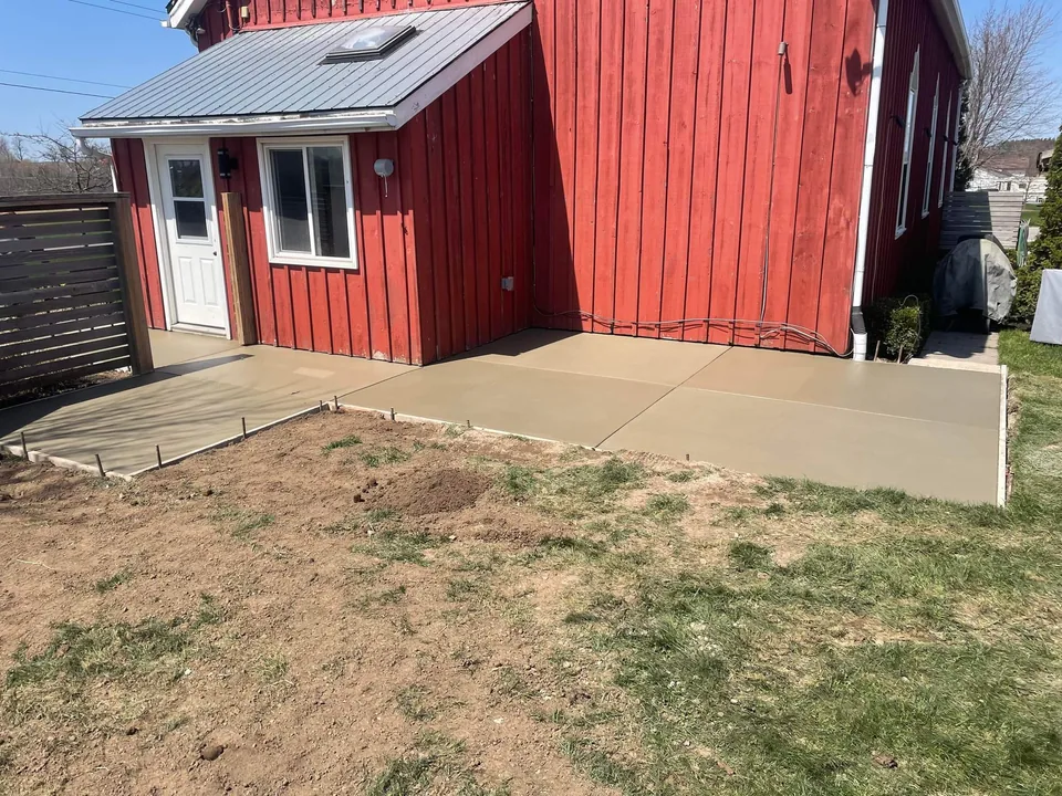 A newly placed concrete path wraps around the side and entrance of a red timber-sided building.