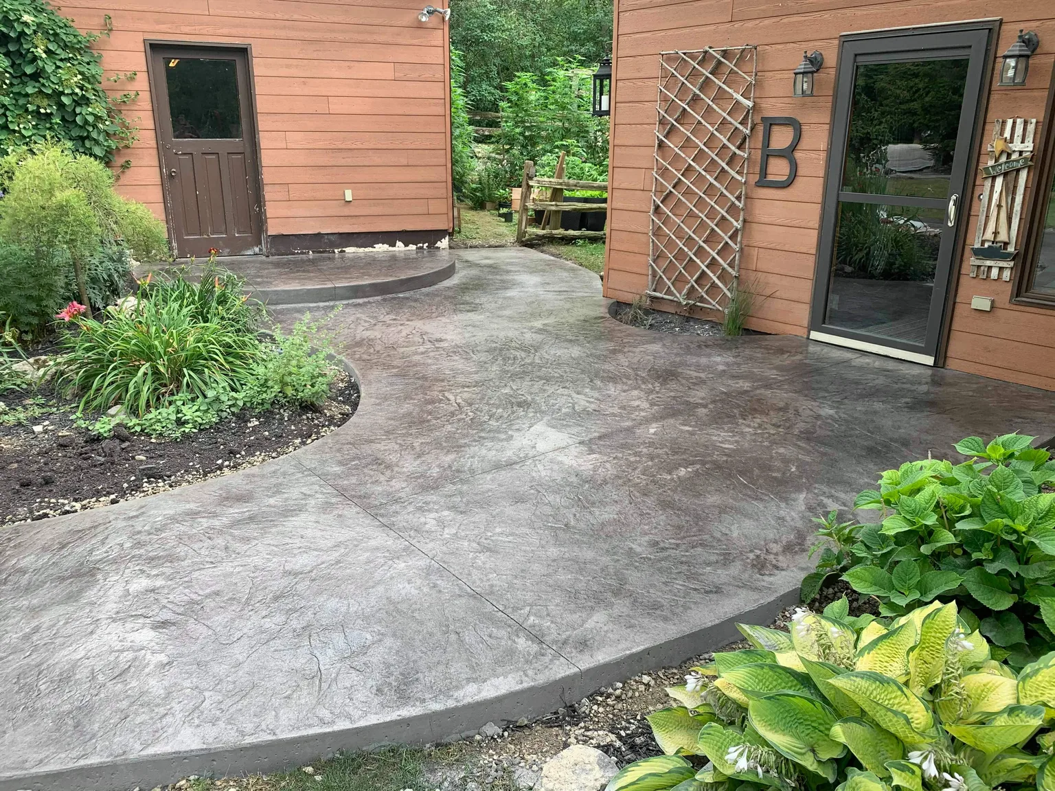 Stamped concrete walkway curving between cedar-sided buildings and garden beds.