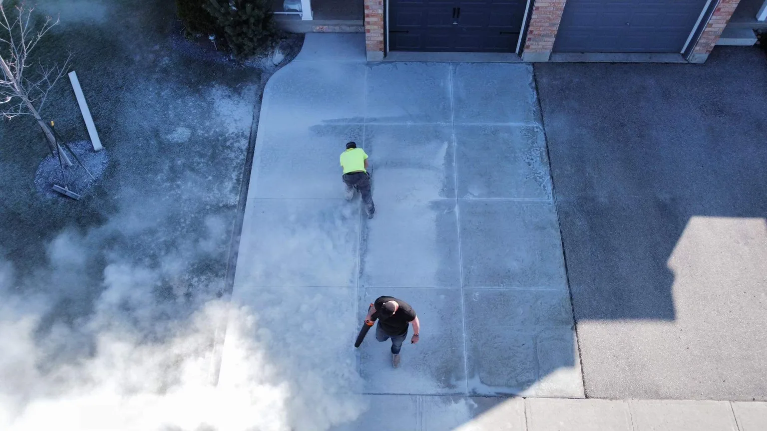 A crew member finishing a concrete driveway beside a home.
